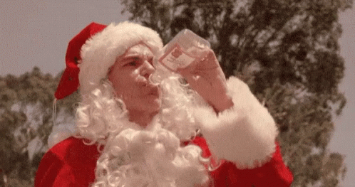A Man Dressed As Santa Claus Is Drinking Water From A Glass . GIF