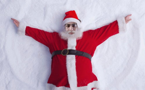 A Man Dressed As Santa Claus Is Laying On The Snow GIF