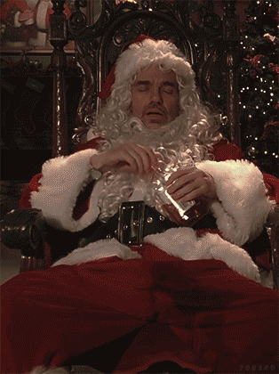 A Man Dressed As Santa Claus Sits In A Chair Holding A Glass GIF