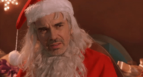 A Man Dressed As Santa Claus With The Words What The Fuck Behind Him GIF