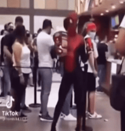 A Man Dressed As Spider Man Is Standing In Front Of A Crowd Of People . GIF