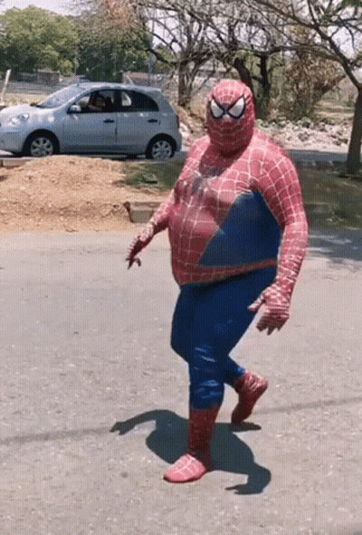 A Man Dressed As Spider Man Is Walking Down The Street GIF