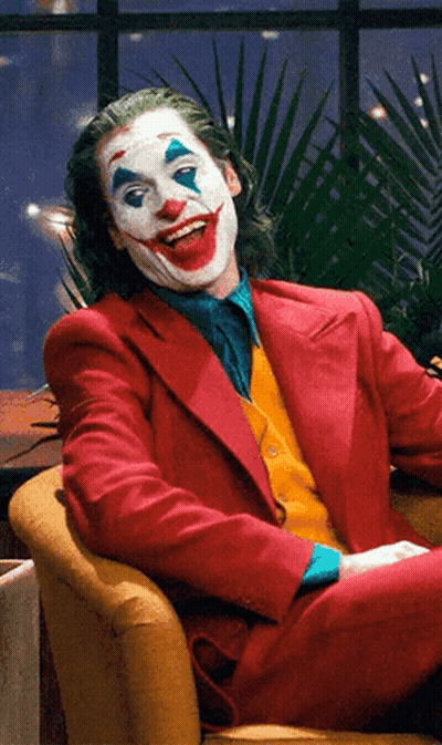 A Man Dressed As The Joker Sits In A Chair GIF