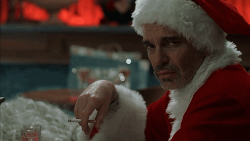 A Man Dressed In A Santa Claus Outfit Is Smoking A Cigarette GIF