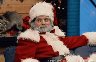 A Man Dressed Up As Santa Claus Is Sitting On A Couch GIF