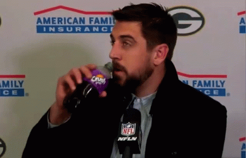 A Man Drinking From A Crush Bottle In Front Of An American Family Insurance Banner GIF