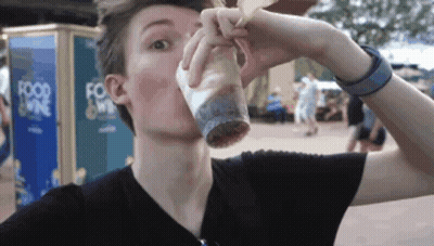 A Man Drinking From A Cup In Front Of A Food Kiosk GIF