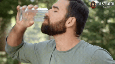A Man Drinking Water From A Glass With A Dr. Squatch Logo On The Bottom GIF