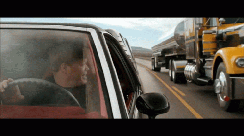 A Man Driving A Car On A Highway Next To A Semi Truck That Says Peterbilt On It GIF