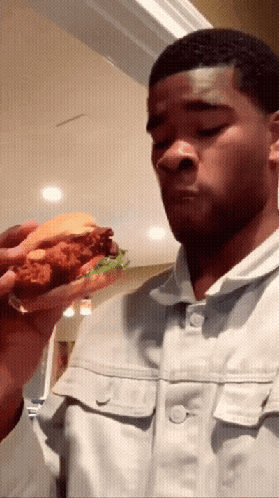 A Man Eating A Fried Chicken Sandwich With Lettuce GIF