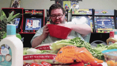 A Man Eating A Salad In Front Of A Mortal Kombat Video Game GIF