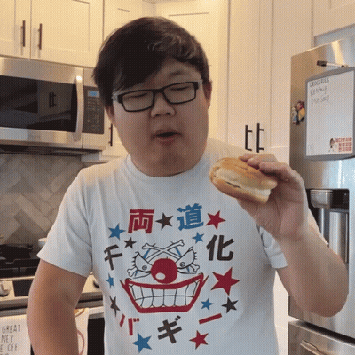 A Man Eating A Sandwich In Front Of A Refrigerator With Groceries On It GIF