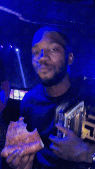 A Man Eating A Slice Of Pizza While Wearing A Ufc Championship Belt GIF