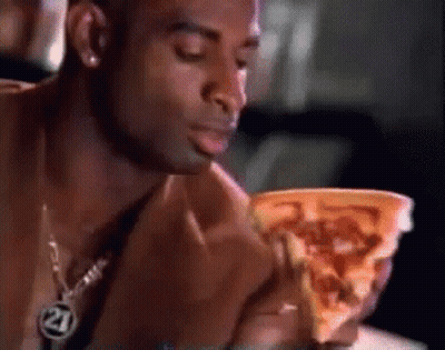 A Man Eating A Slice Of Pizza With The Number 21 On His Necklace GIF