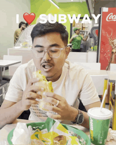 A Man Eating A Subway Sandwich And Drinking A Soda GIF