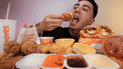 A Man Eating Fried Chicken From A Paper Bag That Says Cajun French Fries GIF