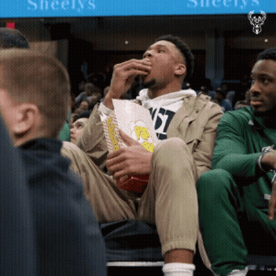 A Man Eating Popcorn In Front Of A Sign That Says Sheelys GIF