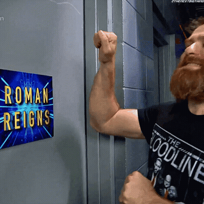 A Man Flexes His Arm In Front Of A Roman Reigns Sign GIF