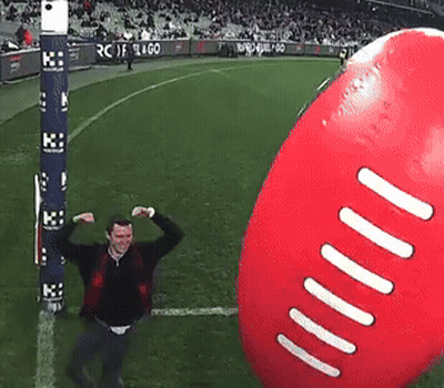 A Man Flexes His Muscles In Front Of A Giant Football GIF
