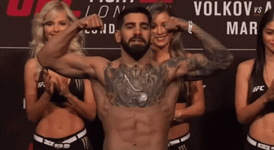 A Man Flexes His Muscles In Front Of A Sign That Says Volkov On It GIF
