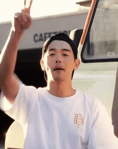 A Man Giving A Peace Sign In Front Of A Building That Says Cafe On It GIF