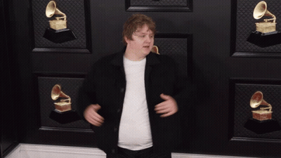 A Man Giving A Thumbs Up In Front Of A Wall With Grammophone Trophies GIF