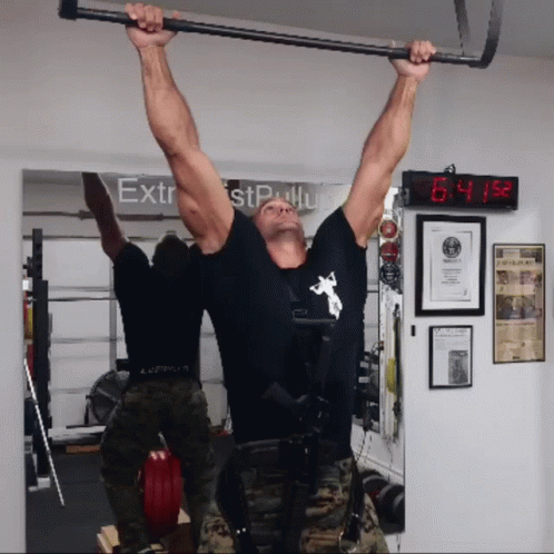 A Man Hangs Upside Down In Front Of A Sign That Says Extrest Pull Up GIF