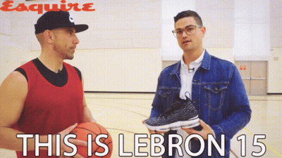 A Man Holding A Basketball Talks To Another Man Who Is Holding A Pair Of Lebron 15 Sneakers GIF