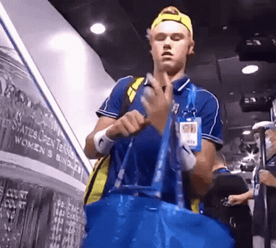 A Man Holding A Blue Bag In Front Of A Wall That Says ' United States Open Tennis ' On It GIF