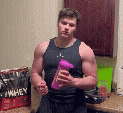 A Man Holding A Bottle In Front Of A Bag That Says 100 % Whey GIF