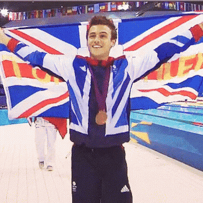 A Man Holding A British Flag With His Arms Outstretched And A Medal Around His Neck GIF