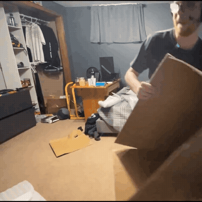 A Man Holding A Cardboard Box In A Messy Room With A Shirt That Says " I Love You " GIF