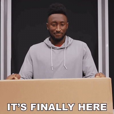 A Man Holding A Cardboard Box With The Words " It 'S Finally Here " Above Him GIF
