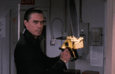 A Man Holding A Chainsaw In Front Of A Sign That Says Exit GIF