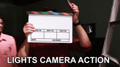 A Man Holding A Clapper Board With The Words Lights Camera Action GIF