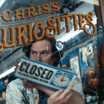 A Man Holding A Closed Sign In Front Of Chris 'S Curiosities Sign GIF