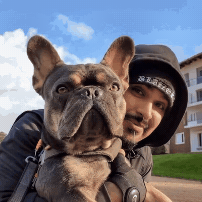 A Man Holding A Dog Wearing A Black Beanie That Says Blaze GIF