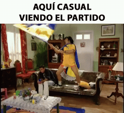 A Man Holding A Flag In A Living Room With The Words Aqui Casual Viendo El Partido On The Bottom GIF