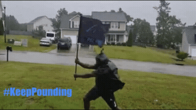 A Man Holding A Flag In The Rain With #Keeppounding Written In Blue GIF