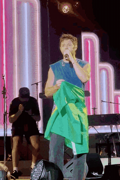 A Man Holding A Green And Yellow Flag On Stage GIF