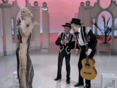 A Man Holding A Guitar Is Standing Next To A Woman Singing GIF