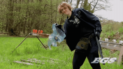 a man holding a gun in a field with the word bgs on the bottom right
