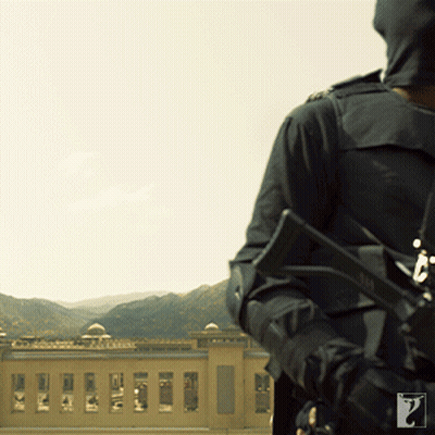 A Man Holding A Gun In Front Of A Building And Mountains GIF
