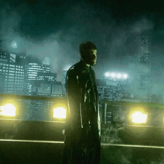 A Man Holding A Gun Stands In Front Of A City At Night GIF