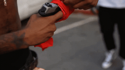 A Man Holding A Gun With A Red Bandana Around His Thumb GIF