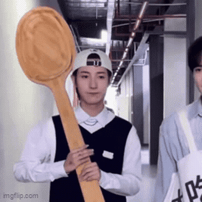 A Man Holding A Large Wooden Spoon In A Hallway . GIF