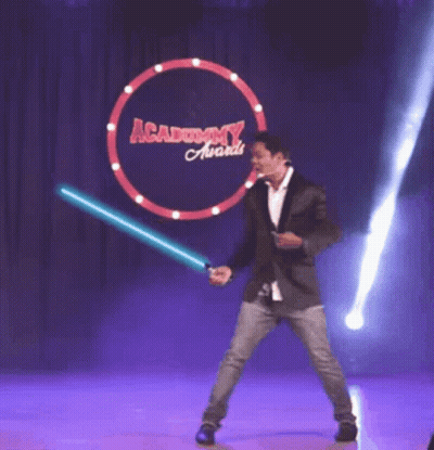 A Man Holding A Light Saber In Front Of An Academy Award Sign GIF