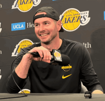 A Man Holding A Microphone In Front Of A Lakers Logo GIF