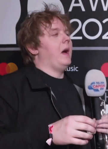 A Man Holding A Microphone In Front Of A Sign That Says Music GIF