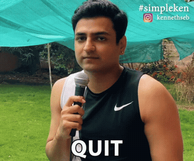 A Man Holding A Microphone With The Word Quit Written On His Shirt GIF